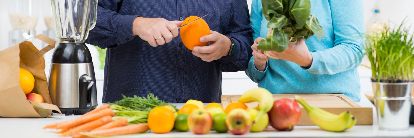 Ein Mann und eine Frau sind in einer Küche, sie bereiten Obst und Gemüse zu. 