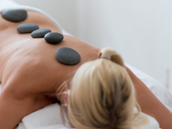 Eine Frau liegt auf einer Behandlungsliege, sie bekommt eine La-Stone-Therapie. Bei der Therapie werden auf ihren Rücken aufgeheizte Steine gelegt. 