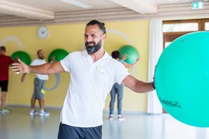 In einem Sport- Gesundheitskurs zeigt ein Physiotherapeut eine Sportübung mit einem Gymnastikball 